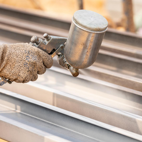 Industrial-Powder-Coating-Applied-to-Metal عامل يقوم برش طلاء البودرة على عوارض معدنية – يعبر عن خدمات التشطيب والحماية من التآكل في مؤسسة ASC